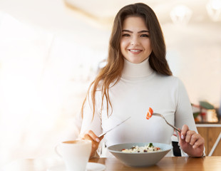 young beautiful smiling woman biting peace of tomatoe while eating salad in cafe during lunch time, food and drink concept