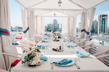 A rooftop restaurant overlooking the city. Festive table served dishes and decorated with flowers for wedding party. Image of celebrate outdoor party on background town.