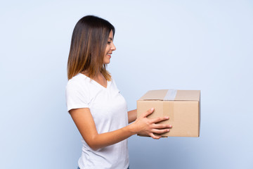 Young woman over isolated blue background holding a box to move it to another site