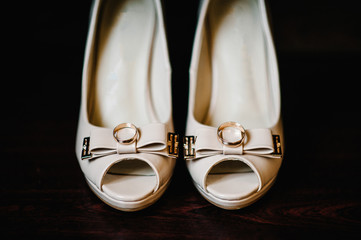 Wedding accessory bride. Stylish lacquered white shoes, gold rings are isolated standing on brown...