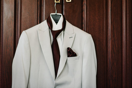 A man's jacket, white suit with tie on a hanger on the background brown wooden wall in the room. - Powered by Adobe