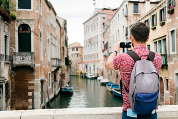 Fototapeta na wymiar Young traveler taking a photo with his smartphone of a canal in Venice, Italy