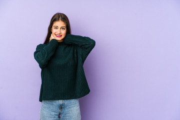 Young caucasian woman isolated on purple background touching back of head, thinking and making a choice.