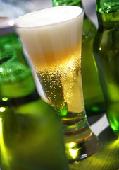 ein Glas Bier frisch eingegossen und grüne Bierflaschen 