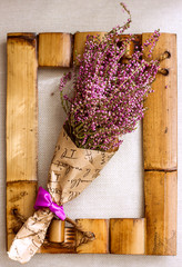 Heather bouquet in paper packaging on a background of vintage aged wooden defocused frame, interior decoration decorative frame from bamboo