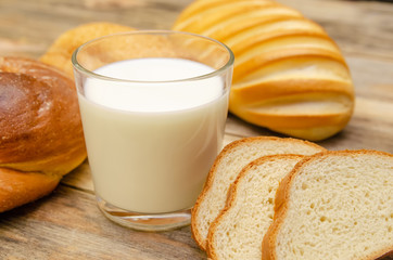 Glass of milk, rolls, sliced loaf on a wooden background