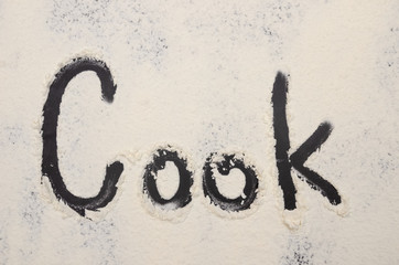 words Cook written on a black background with flour. Inscription.
