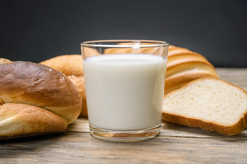 Glass of milk, rolls, sliced loaf on a wooden background