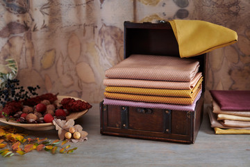 Wooden chest with stack of hand-dyed fabrics, wooden plate with autumn leaves, nuts and berries on an eco-print background