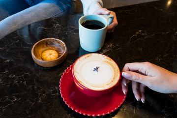 Red cup of hot cappuccino in female hand on wooden table