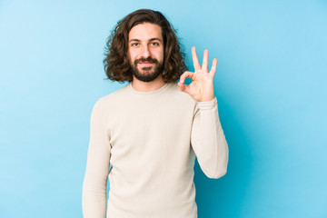 Young long hair man isolated on a blue background cheerful and confident showing ok gesture.