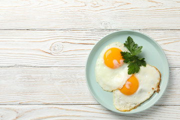 Plate with fried eggs on wooden background, top view
