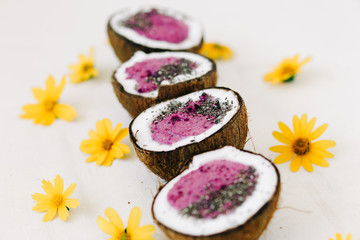 a plates of natural coconut shell with a healthy Breakfast green buckwheat smoothie with berries and Chia seeds and yellow flowers