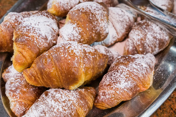 Classic french croissants with icing sugar on silver plate.