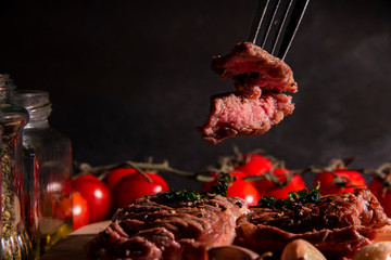 Medium sized homemade grilled steak, sliced ​​on a chopping block, appetizing with rosemary and spices, dark background, top view, restaurant business concept