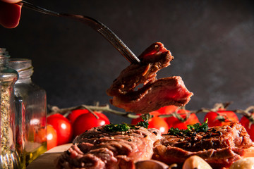 Medium sized homemade grilled steak, sliced ​​on a chopping block, appetizing with rosemary and spices, dark background, top view, restaurant business concept