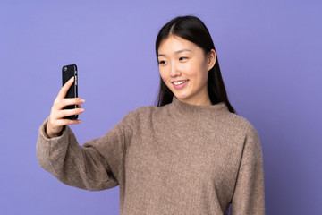 Young asian woman isolated on purple background making a selfie