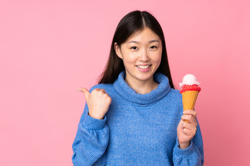 Young asian woman with a cornet ice cream isolated on pink background pointing to the side to present a product