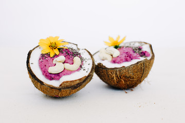 healthy Breakfast berry smoothie with Chia seeds and cashew nuts in a natural coconut plate decorated with yellow flowers on a white table