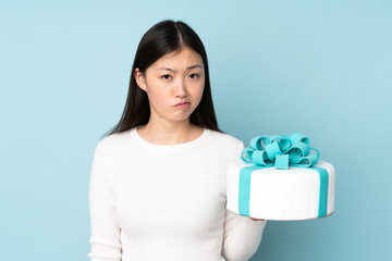 Pastry asian chef holding a big cake isolated on blue background with sad expression