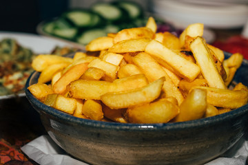French fries served on a plate on table with blurred cucumbers on background, close-up.