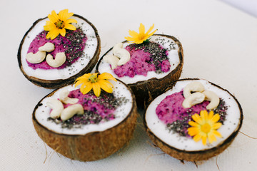 healthy Breakfast berry smoothie with Chia seeds and cashew nuts in a natural coconut plate decorated with yellow flowers on a white table