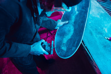 Skater in process of making his own skateboard, longboard - open business concept. Neon lighted studio of creating skateboards. Concept of openspace, craft production, workshop. Polishes, paints. © master1305