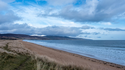 Brora beach on a calm spring morning, with blue skies and clouds and with people walking the beach in the distance