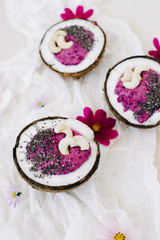 healthy Breakfast berry smoothie with Chia seeds and cashew nuts in a natural coconut plate on a white table with pink flowers