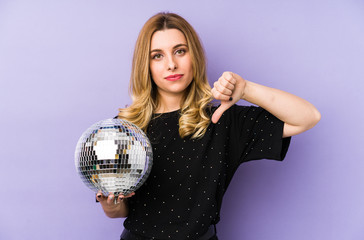 Young blonde woman holding a night party ball isolated showing a dislike gesture, thumbs down. Disagreement concept.