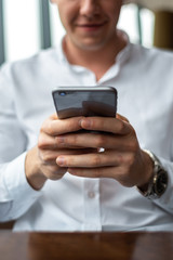 Closeup of a young businessman hands wearing a white fashion shirt chatting on a mobile cell phone in a cafe with a laptop. Freelance and selfemployment concept. Distance dream job.