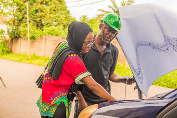 young african man, a professional mechanic, using a laptop to fix and detect fault in a car for a lady