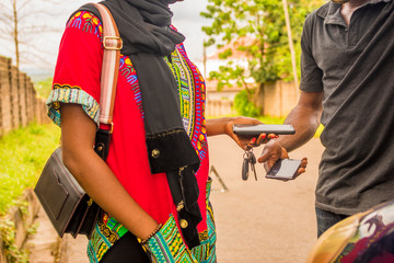 young african woman paying a mechanic who helped fixed her car via mobile transfer