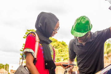 young african woman paying a mechanic who helped fixed her car via mobile transfer