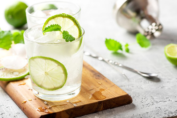 Cold refreshing drink in a glass with lime slices, mint and ice cubes. Summer lemonade with citrus close-up.