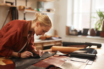 Fototapeta na wymiar Horizontal shot of young Caucasian woman preparing leather materials for new craftwork in her workshop