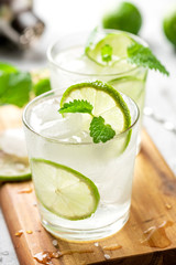 Cold refreshing drink in a glass with lime slices, mint and ice cubes. Summer lemonade with citrus close-up.