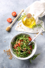 The concept of healthy food. Leaf salad with grits and pine nuts in a deep bowl. Arugula, spinach, tomatoes, spelt, olive oil, honey on a light background. Background image, copy space