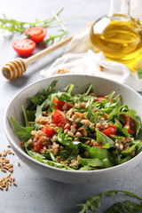 The concept of healthy food. Leaf salad with grits and pine nuts in a deep bowl. Arugula, spinach, tomatoes, spelt, olive oil, honey on a light background. Background image, copy space