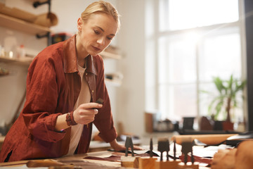 Horizontal shot of young adult beautiful woman wearing casual outfit choosing stitching chisel for further work