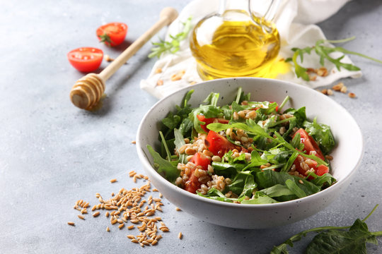 The concept of healthy food. Leaf salad with grits and pine nuts in a deep bowl. Arugula, spinach, tomatoes, spelt, olive oil, honey on a light background. Background image, copy space