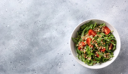 The concept of healthy food. Leaf salad with grits and pine nuts in a deep bowl. Arugula, spinach, tomatoes, spelt on a light background. Background image, copy space