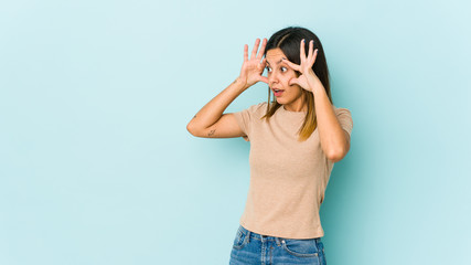 Young woman isolated on blue background keeping eyes opened to find a success opportunity.