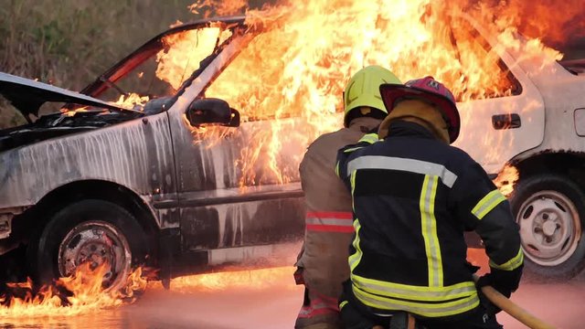 Rear view of Asian fireman wear fire protection suit. Firefighter fighting with fire on a car during fire drill Traffic Accident at Fire station Concept. Slow motion