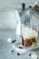 Iced coffee in a tall glass with cream poured over