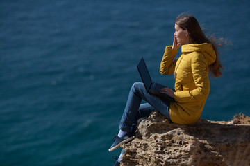 A freelancer girl is working typing on a laptop and talking on a mobile phone with a beautiful view of the open air sea sky. Traveling with a computer. Online dream job.