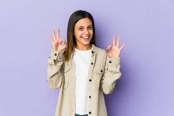 Young woman isolated on purple background cheerful and confident showing ok gesture.