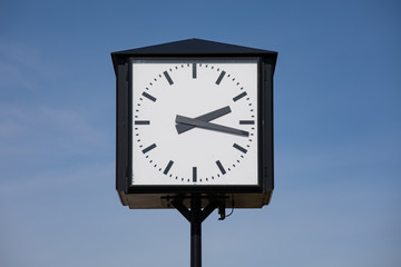 white-black old antique railway station clock with hour and minute hands in front of a blue sky, horizontal format, by day