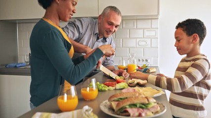 Smiling mixed race family with they son standing in the kitchen preparing sandwich for breakfast at home. - Powered by Adobe