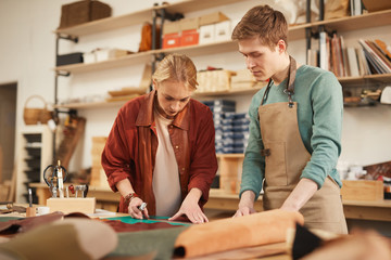 Horizontal medium shot of young Caucasian man and woman working together in modern leather craft workshop